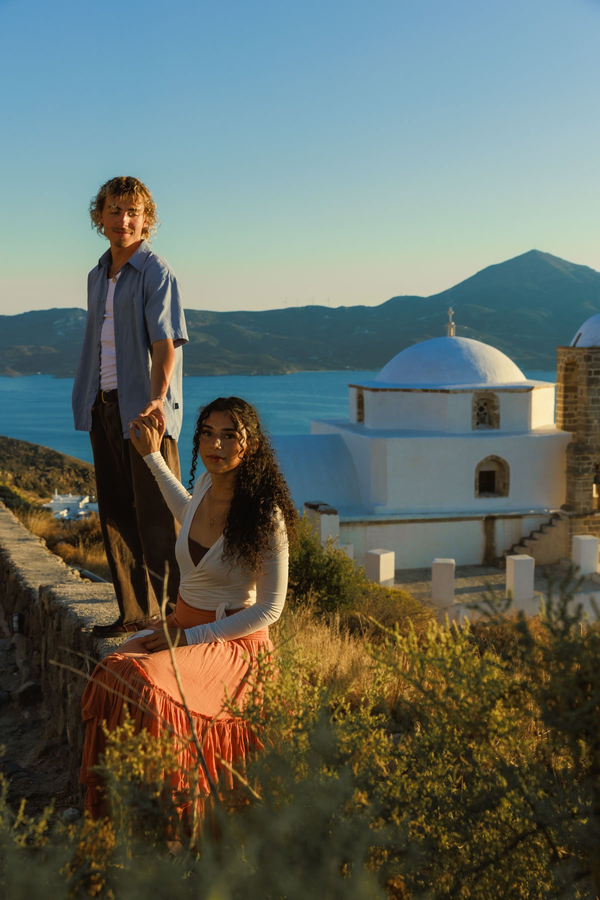 Couple portrait in Milos, Greece at golden hour with a white church and sea in the background