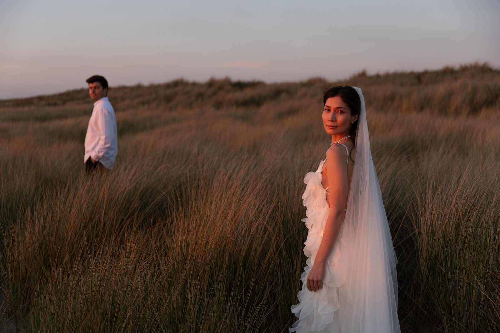 Bride and groom standing in the sand dunes in the Netherlands at sunset